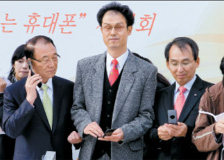 Choi See-joong, KKC chairman, left; Kim Ho-sik, head of welfare at the Hasang Rehabilitation Center, center; and Jung Il-jae, LG Telecom CEO, participate in the demonstration of the โBook2 Reader Mobile Phoneโ yesterday during the World Braille Day celebrations at Namsan Park in Seoul. Provided by the company